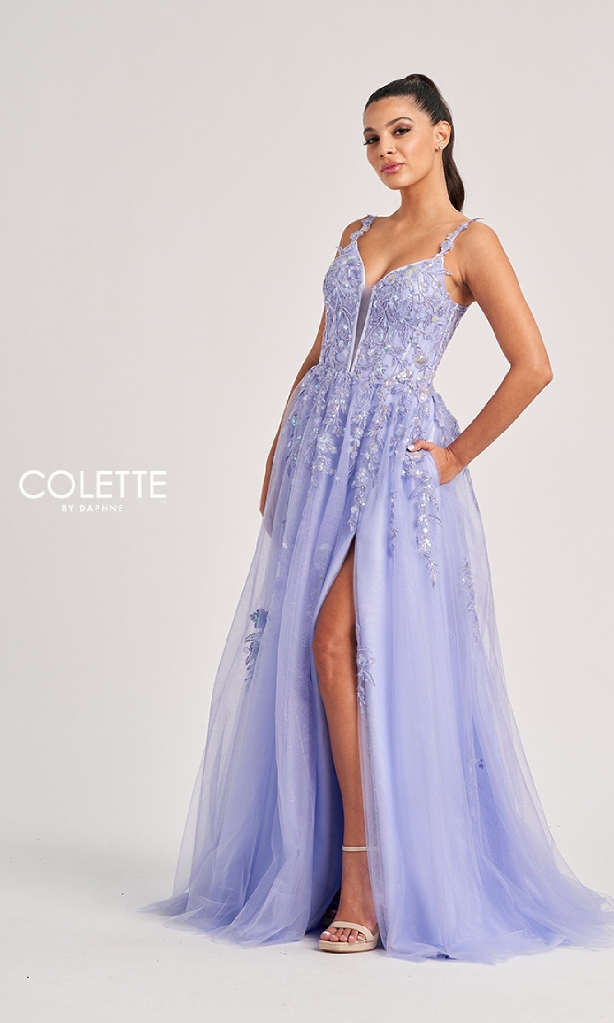 A woman poses in the Colette CL8060 long prom dress, a light purple floral-embellished gown with spaghetti straps and a high slit, against a plain background.